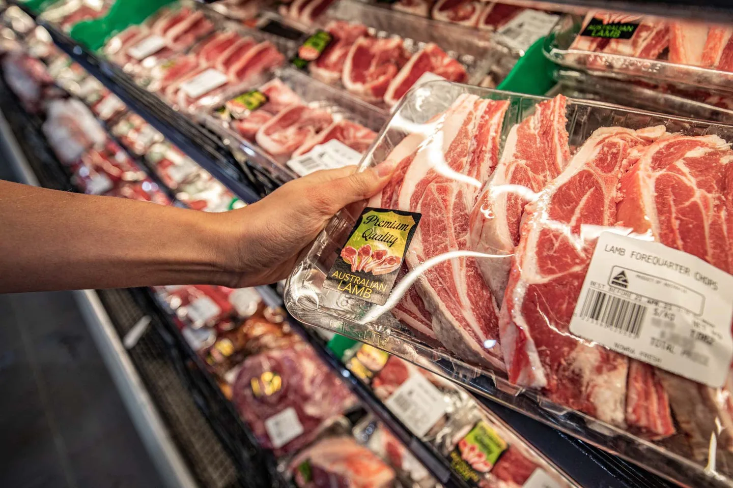 A customer lifting a tray of pork cutlets from the butcher’s cabinet