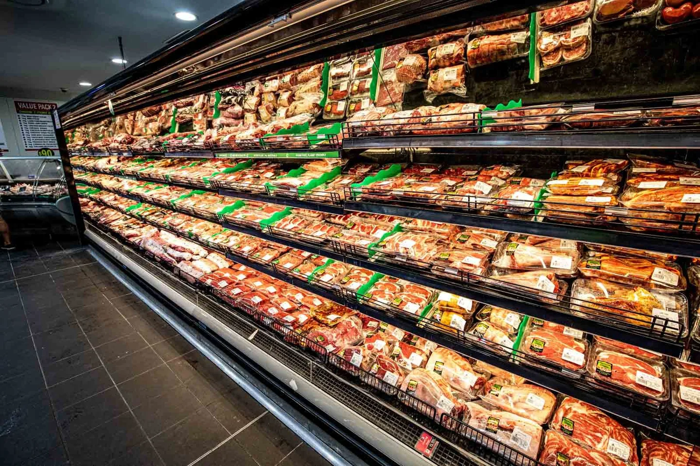 A long refrigerated cabinet filled with trays of pre-packed meat