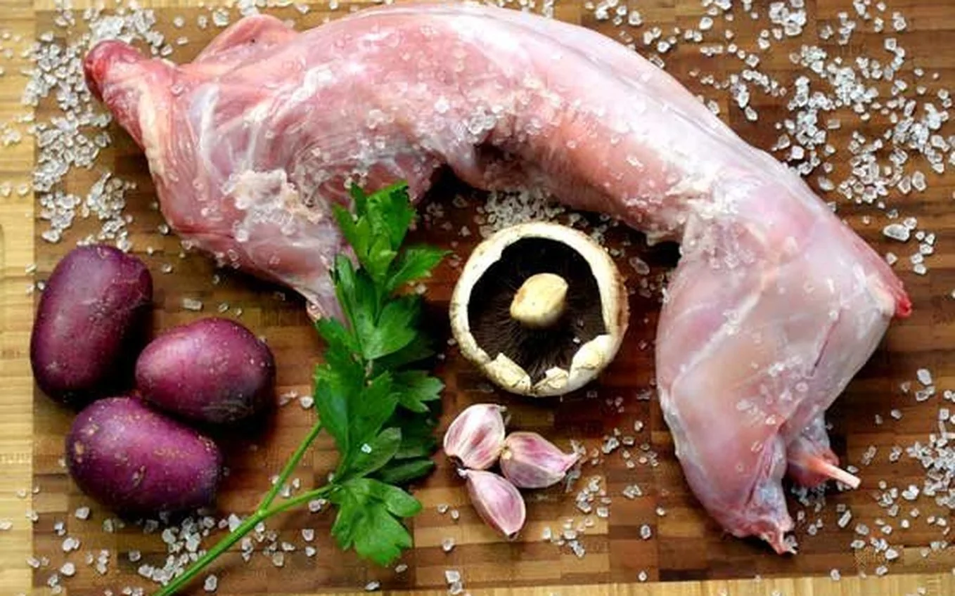 A whole wild rabbit on a board with potatoes, mushroom, garlic and parsley