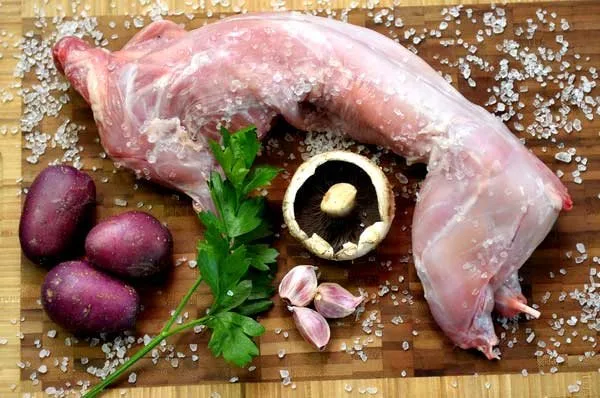 A whole wild rabbit on a board with potatoes, mushroom, garlic and parsley